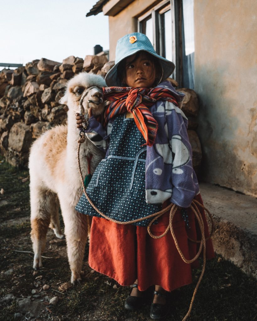 Bolivian girl with baby Llama in Isla del sol, Bolivia. Photo by Alex Azabache on Unsplash